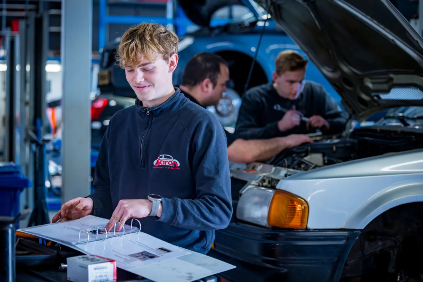 Student Autotechniek zoekt in de werkplaats iets op in een map