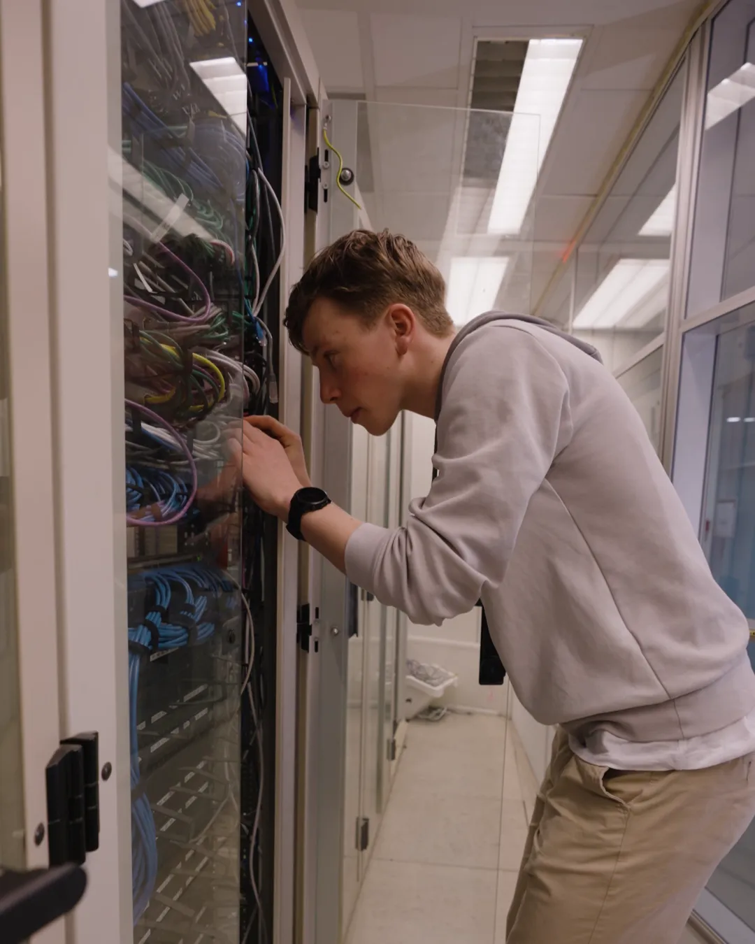 Student sluit kabels aan in een serverkast met veel netwerkkabels tijdens de IT-opleiding.