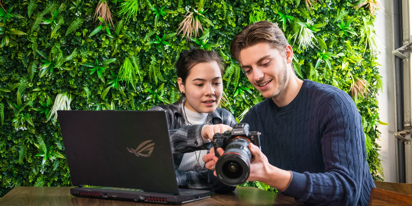 Twee studenten bekijken foto's op een camera met laptop erbij