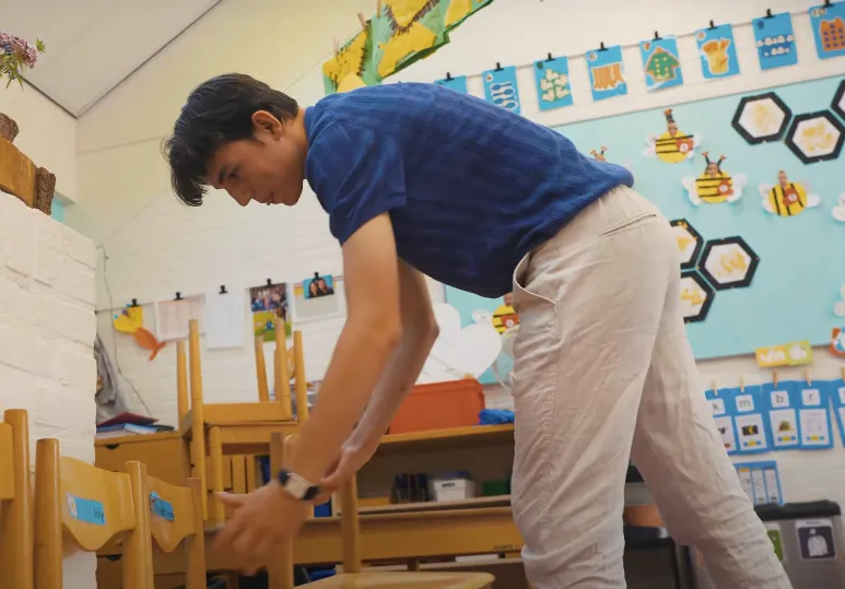 student onderwijsassistent zet stoelen klaar voor basisschoolleerlingen