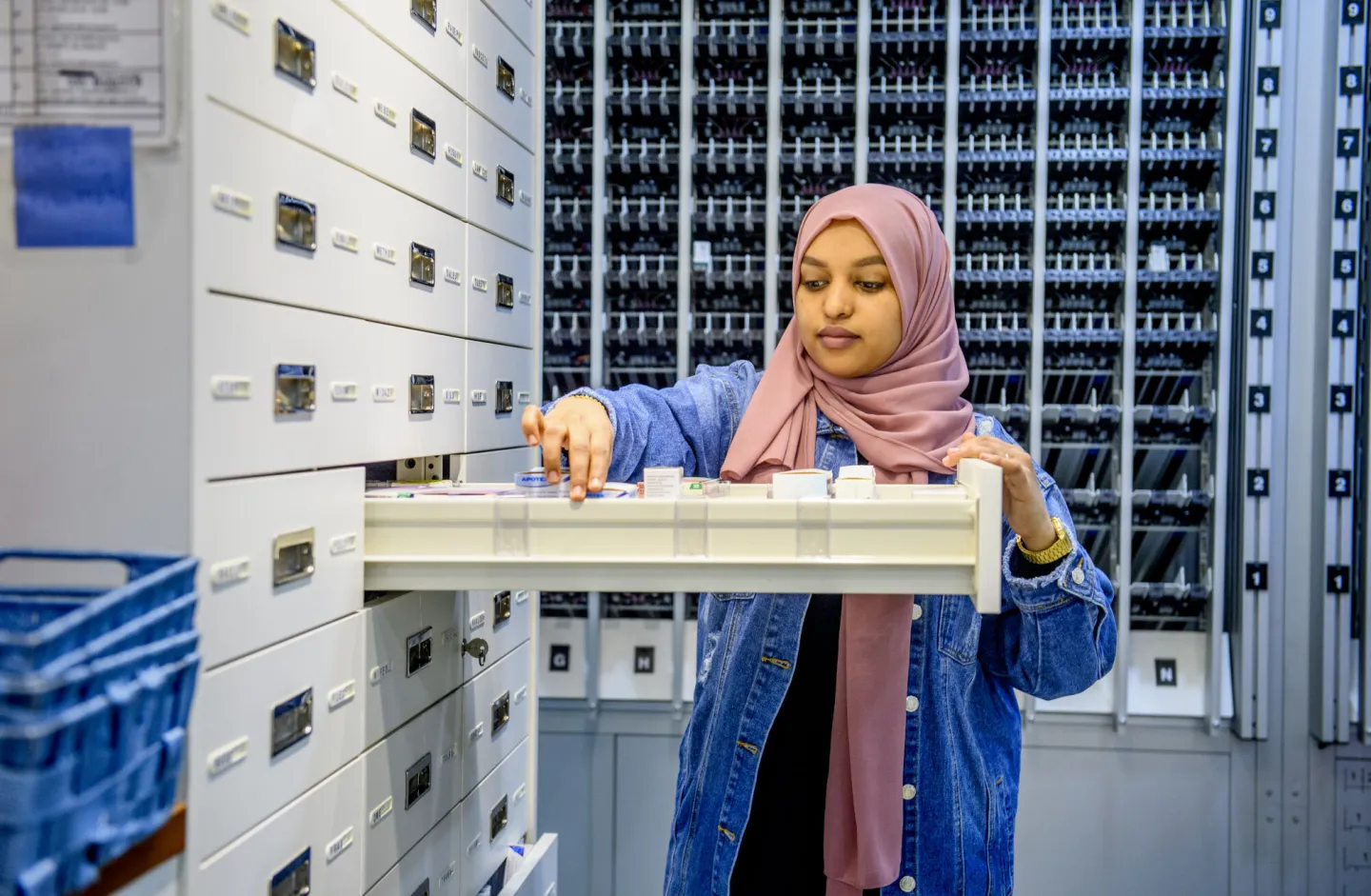 Een vrouw in een hijab kijkt naar een archiefkast in een apotheek.