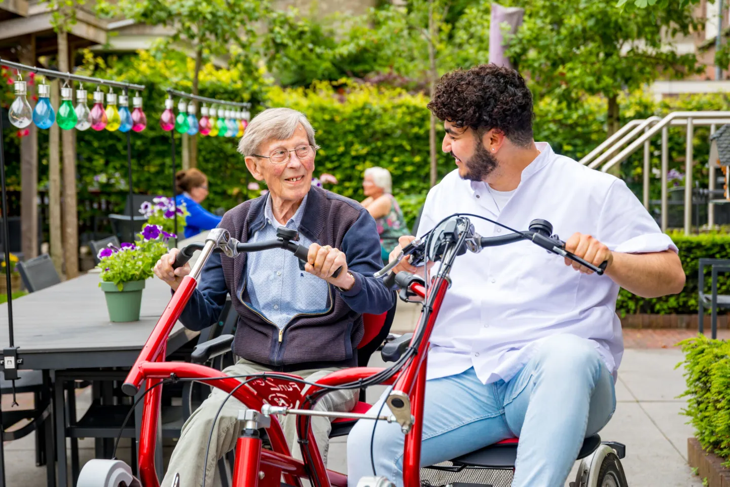 Een oudere man en een jongere man zitten samen op één fiets en vermaken zich uitstekend.