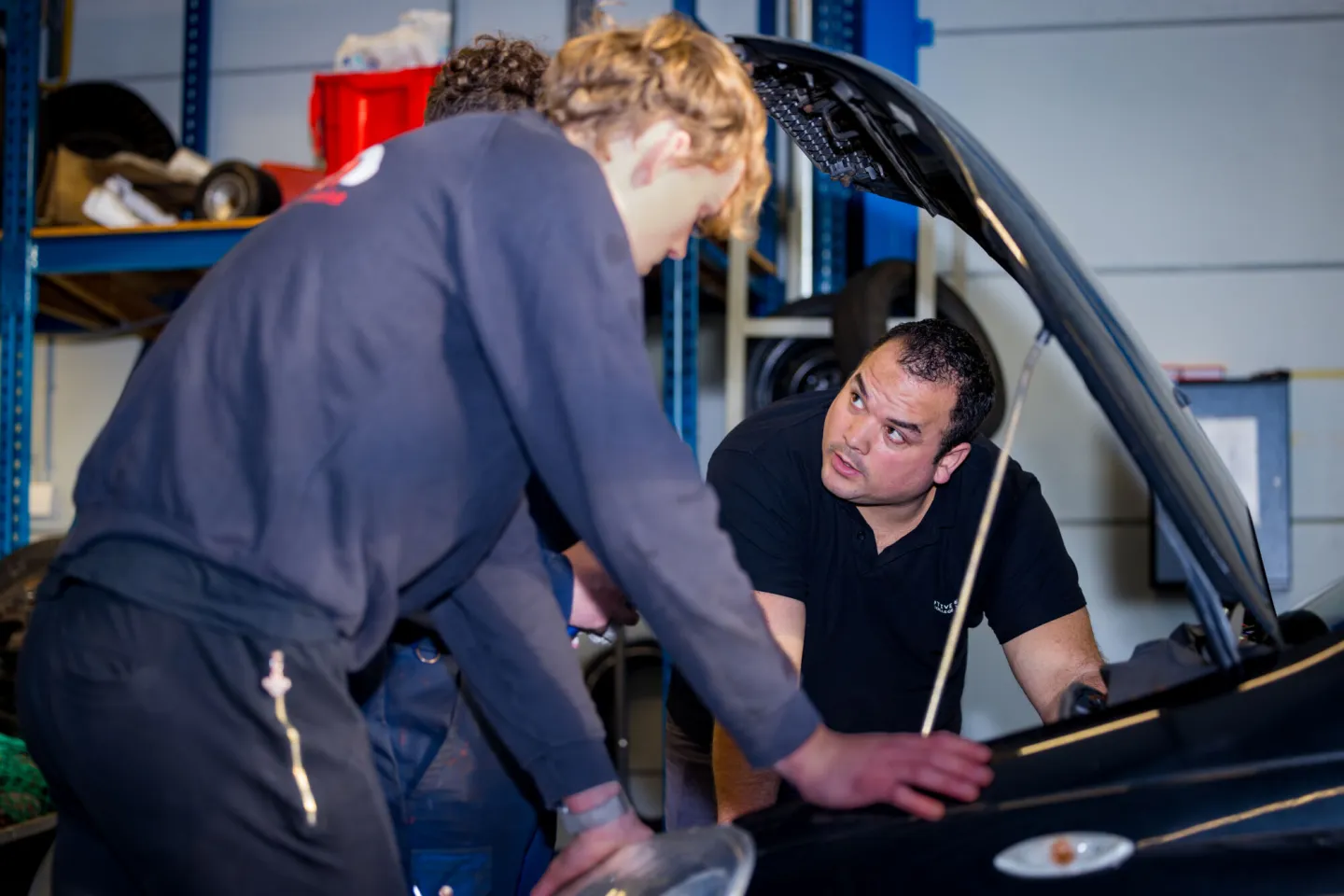 Leidinggevende automotive kijkt onder motorkap auto met twee collega's.