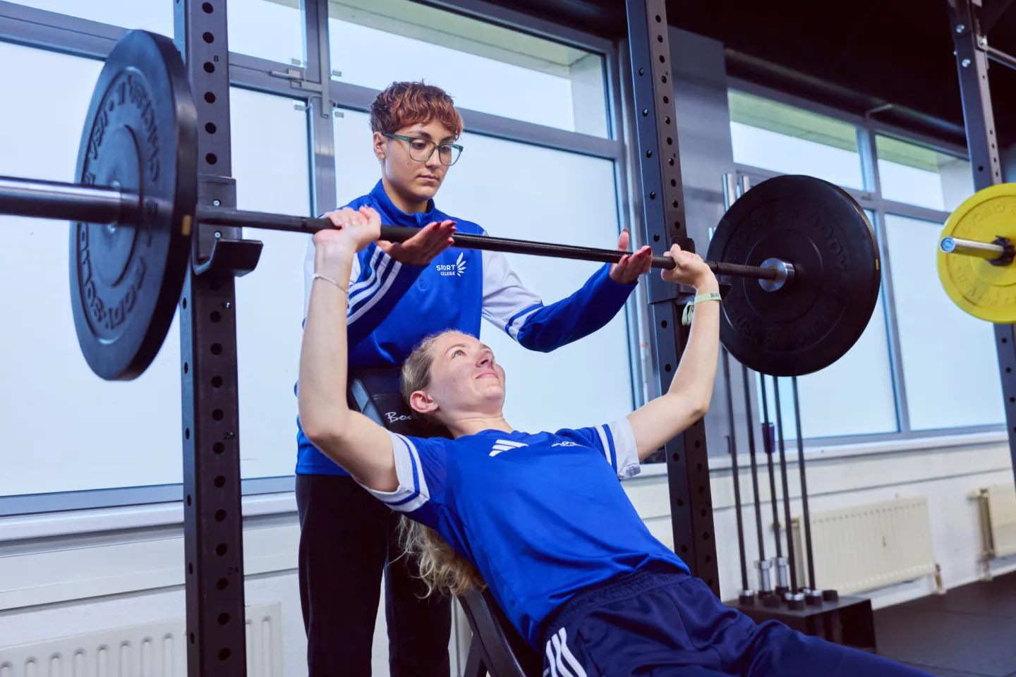 Sportstudent helpt andere sportstudent met gewichtheffen in fitnessruimte