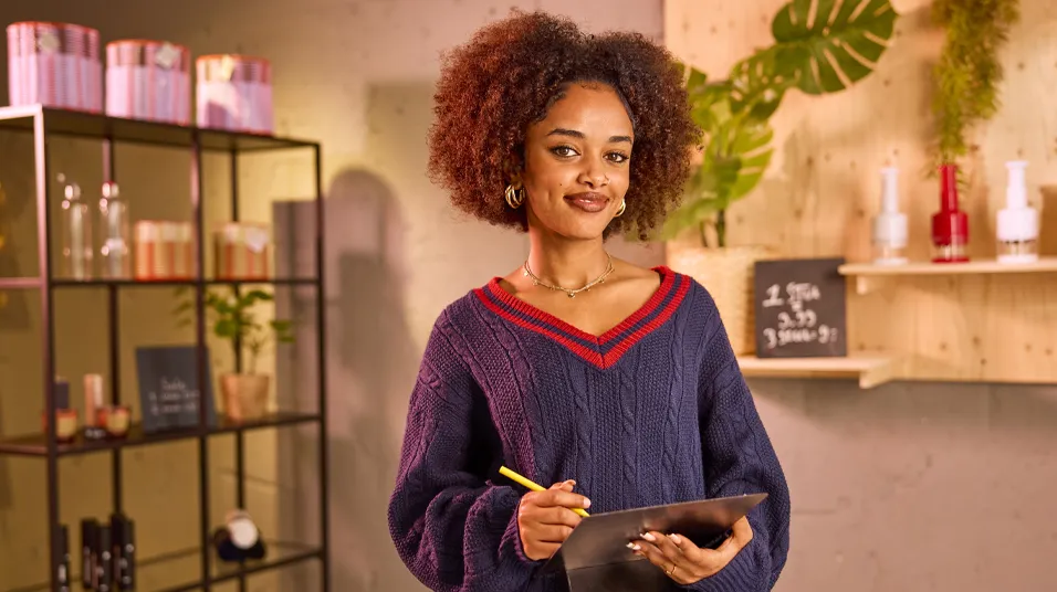 Student in een winkelomgeving maakt notities op een tablet, met producten en schappen op de achtergrond.