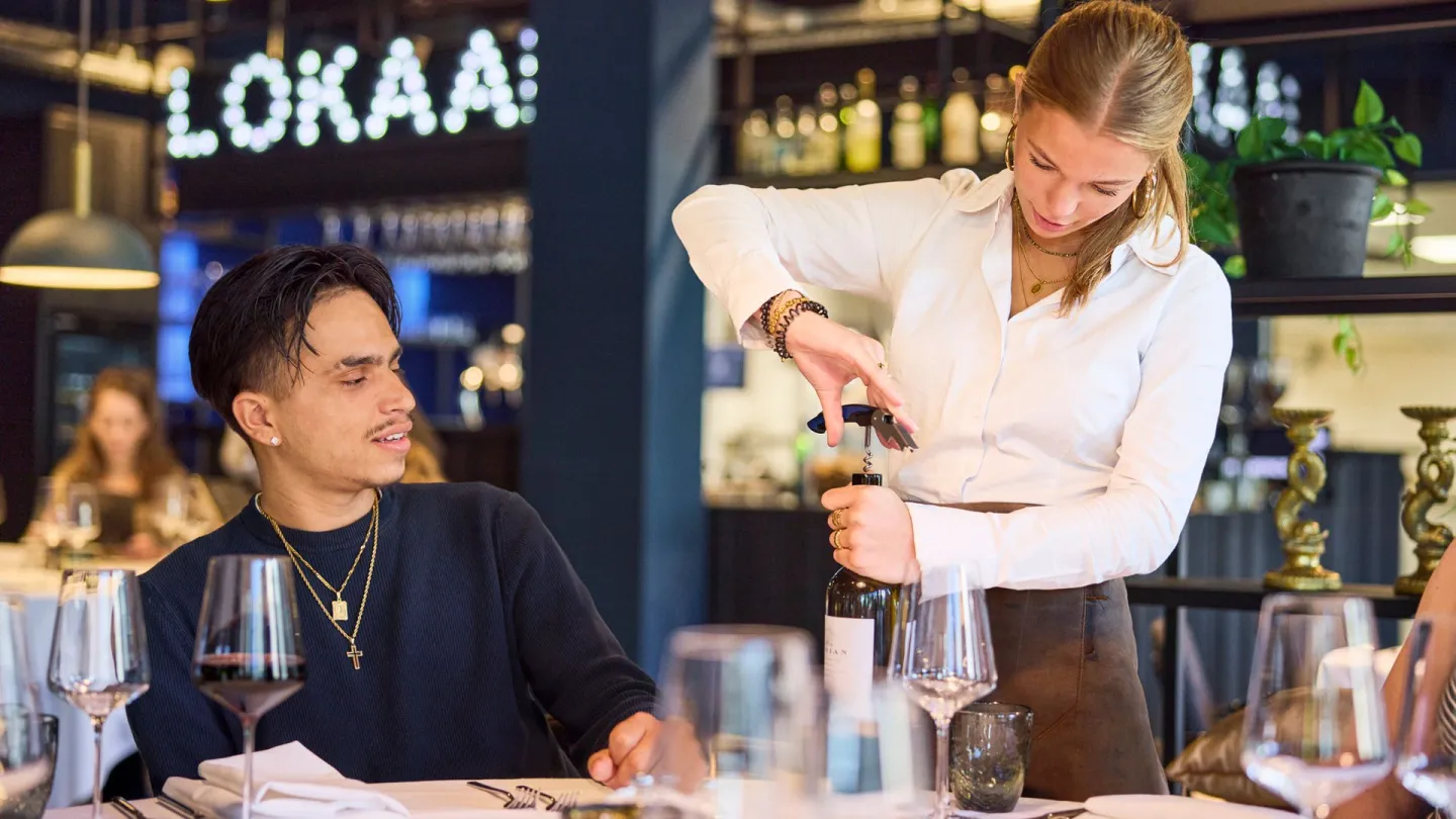 Student Gastheer/Gastvrouw ontkurkt wijn bij leerrestaurant Lokaal