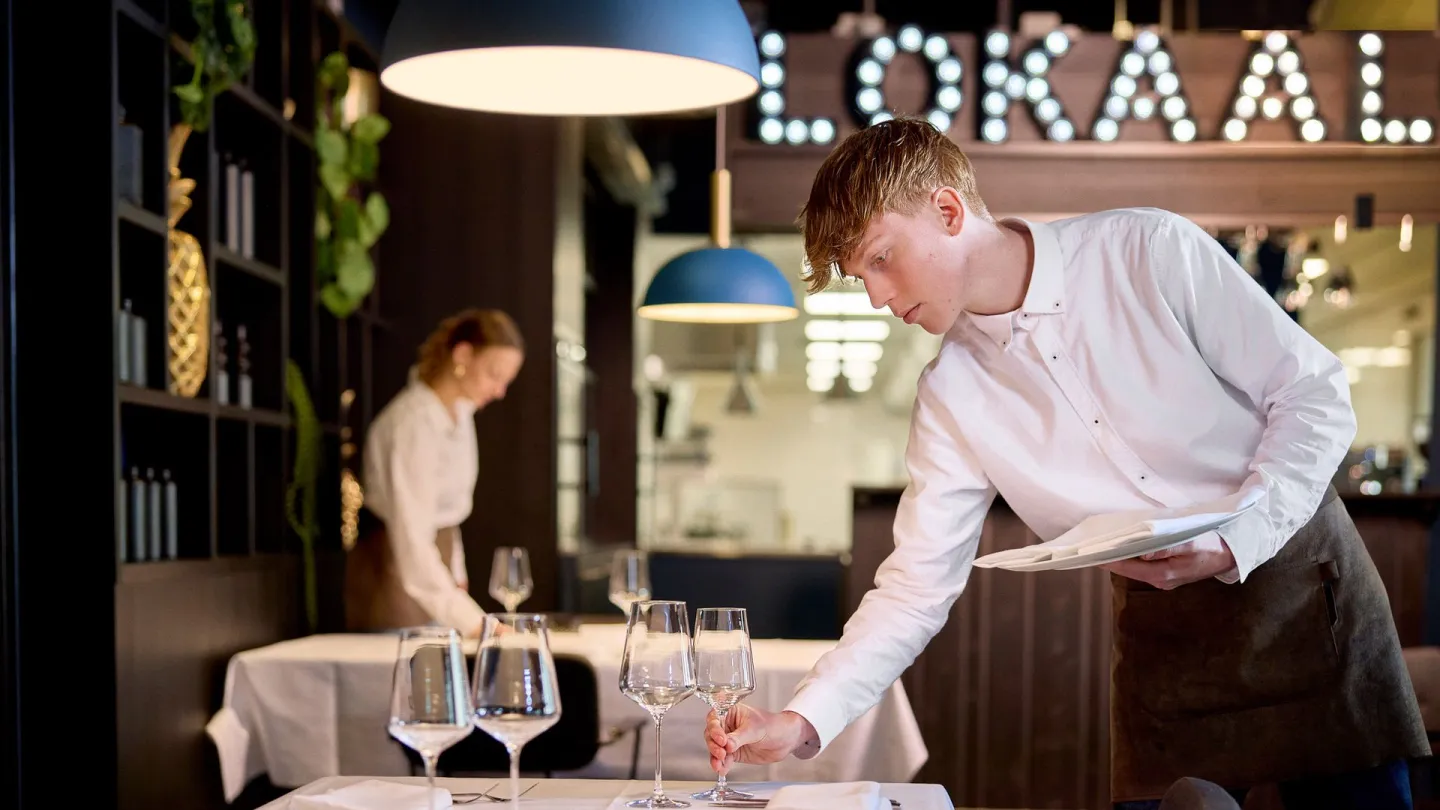Student Gastheer/Gastvrouw zet glazen op tafel in leerrestaurant Lokaal