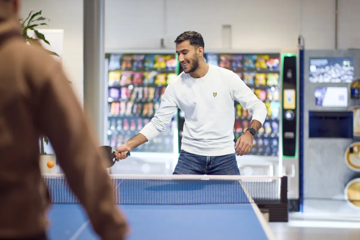 Een student speelt pingpong in een winkel, met een tafel en ballen om hem heen