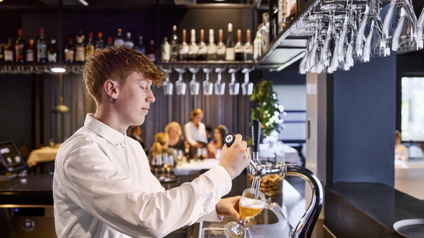 Student Horeca schenkt bier aan bar van leerrestaurant Lokaal