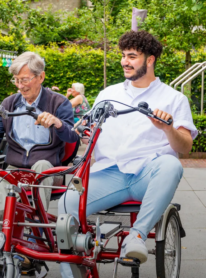 Student helpt oudere man fietsen op duofiets in zorgomgeving