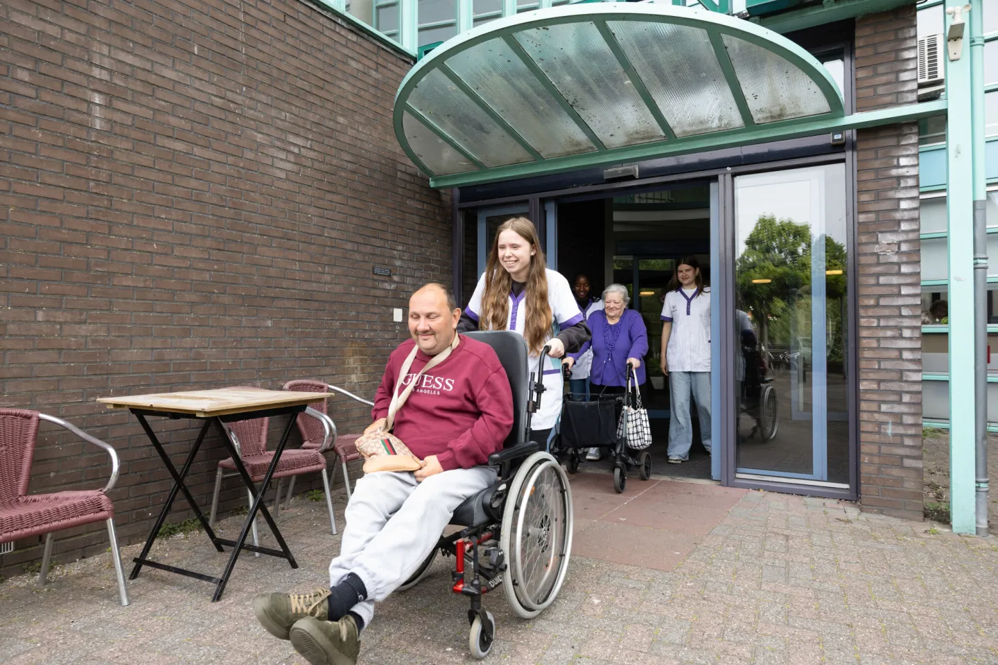 Studenten Flexopleiding Medewerker Helpende Zorg rijdt oudere in rolstoel