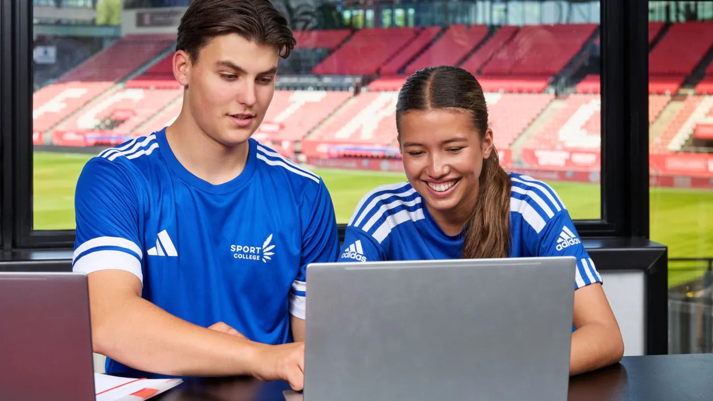 Studenten werken samen achter laptop met Stadion Galgenwaard op achtergrond