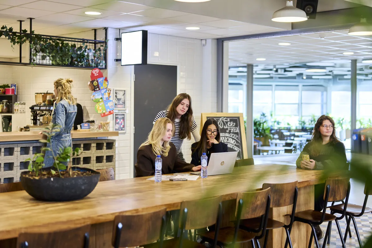 Studenten zitten aan een tafel in de kantine en bespreken iets samen