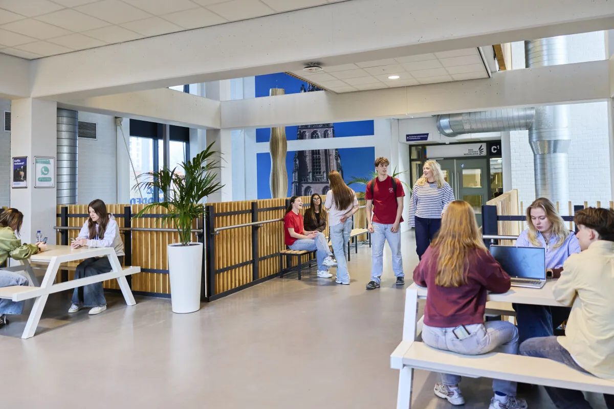 Studenten zitten aan tafels in een grote zaal, met een gezellige sfeer en gesprekken die plaatsvinden