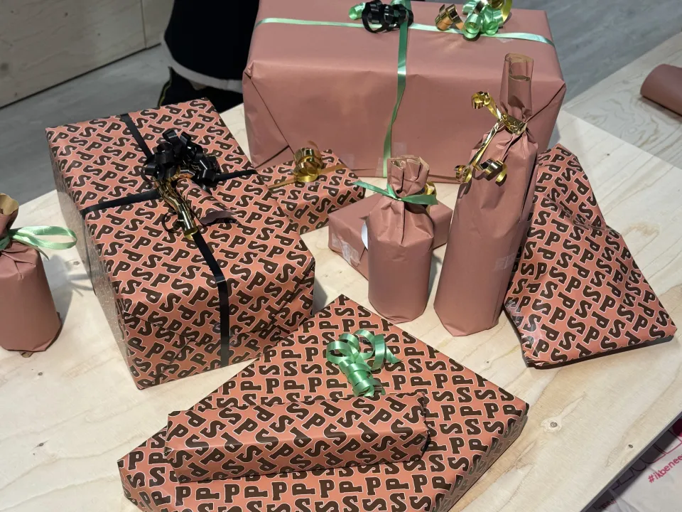 Meerdere ingepakte Sinterklaascadeaus in roze pakpapier met zwarte letters, versierd met linten en strikken op een tafel.