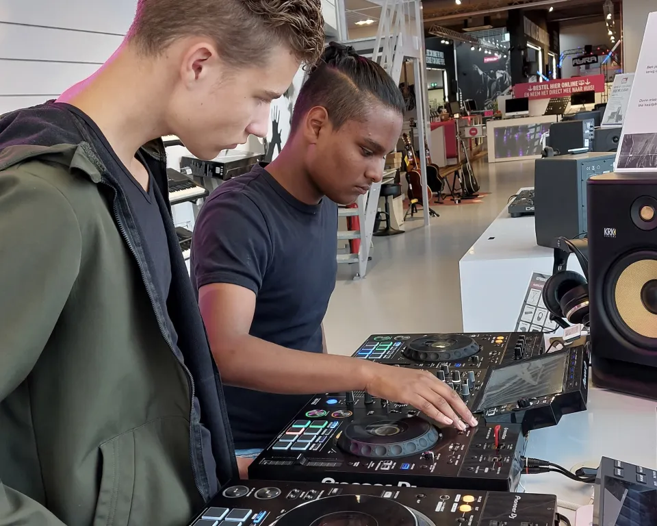 Twee studenten die samen dj-apparatuur uitproberen in een muziekwinkel, terwijl één van hen aan de knoppen draait