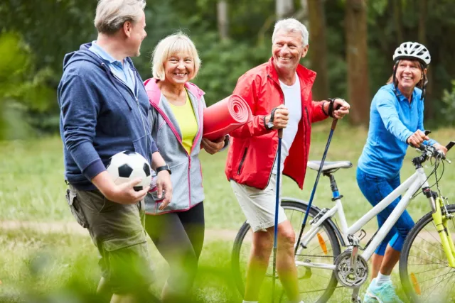 Vier volwassenen die sportief buiten zijn met voetbal, yogamat, Nordic walking sticks en een racefiets.