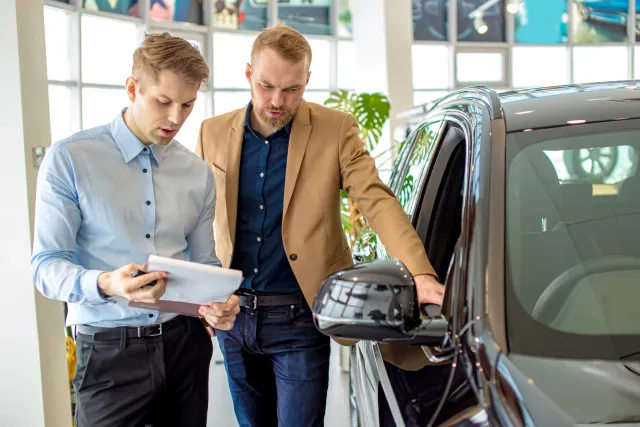 Student en klant bekijken een auto in de showroom van een autodealer