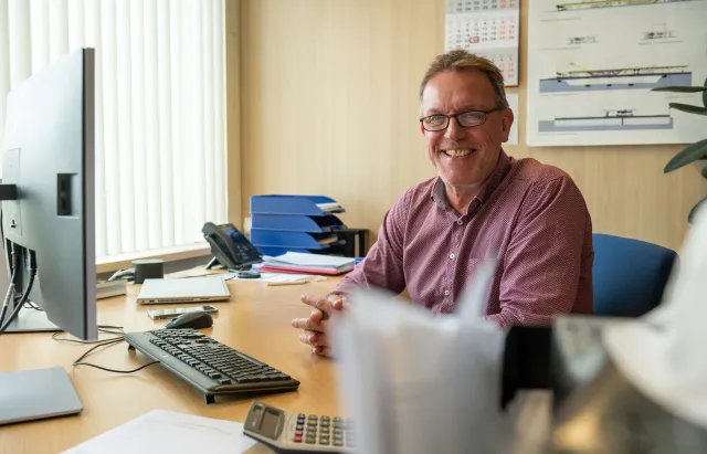 Commercieel medewerker zit aan bureau met computer en kijkt in camera.