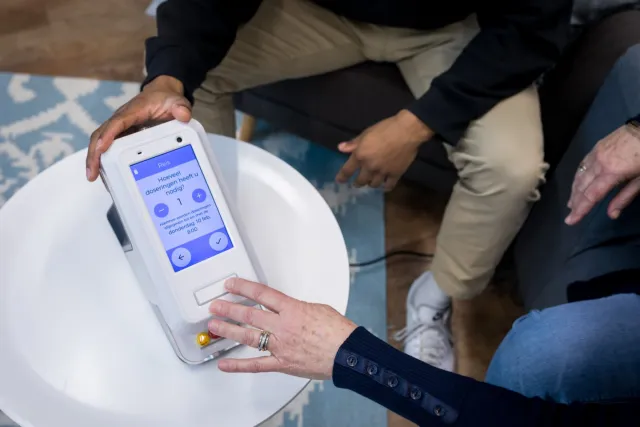 Een hand houdt doseerapparaat voor medicatie vast en andere hand drukt op knopje van apparaat.