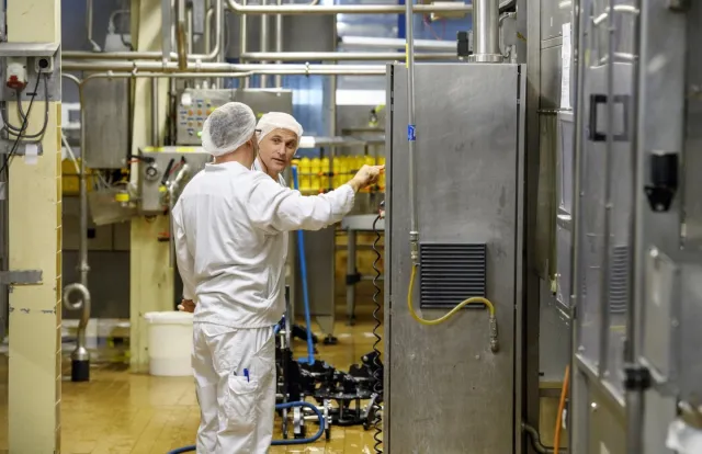 Een student keuzedeel voeding en industriële processen in een machinekamer die op een paneel een controle uitvoert met een praktijkbegeleider. 