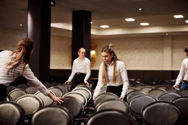 Facilitair dienstverleners zetten stoelen goed in zaal.