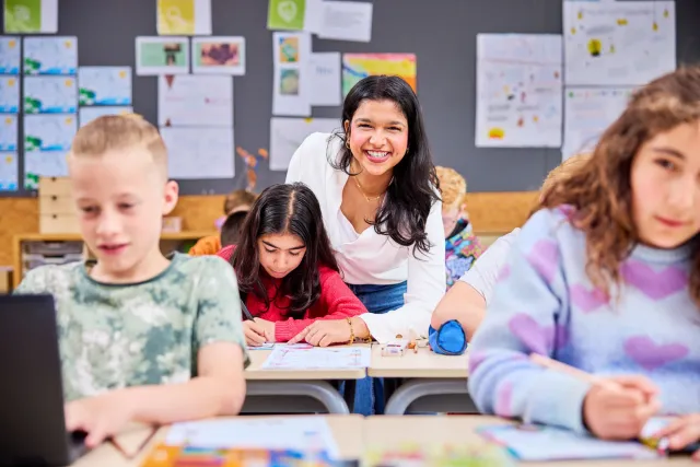 Onderwijsassistent kijkt mee bij schoolwerk basisschoolleerling