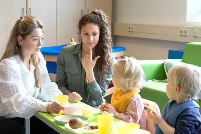 Twee pedagogisch medewerkers helpen twee kinderen bij het eten.