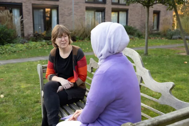 Praktijkopleider in gesprek met medewerker over leertraject buiten op bankje.