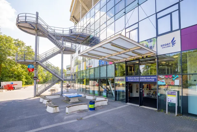Ingang van het Sport College in stadion Galgenwaard in Utrecht met de buitentrap en zitbanken ervoor.