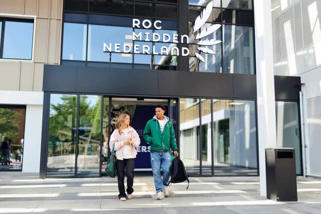 Twee studenten lopen bij de ingang van een schoolgebouw