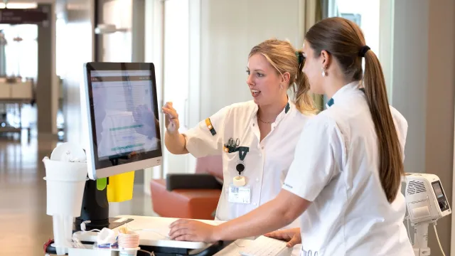 Studenten Verpleegkunde bekijken monitor in ziekenhuisgang.