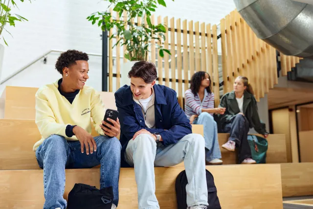Twee studenten zitten samen op een bank en kijken naar een telefoon