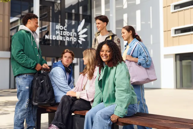 Groep studenten zit en staat buiten voor een schoolgebouw