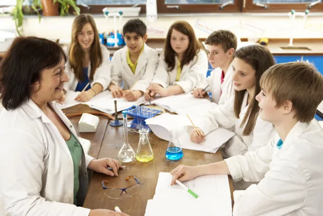 Technisch onderwijsassistent begeleidt zes leerlingen in practicumlokaal.