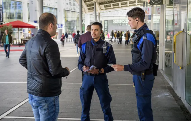Twee handhavers in gesprek met man op straat.