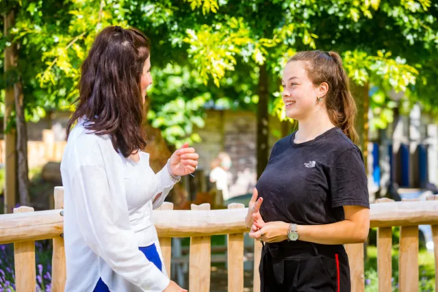 Twee vrouwen praten met elkaar naast een houten hek. 