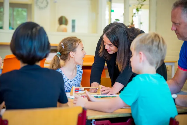 Klaslokaal met leraar en kinderen aan tafel.
