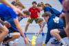 In een gymzaal zijn meerdere leerlingen met een oefening bezig. Achterin staat de docent aan te moedigen en te beoordelen hoe de leerlingen het uitvoeren.