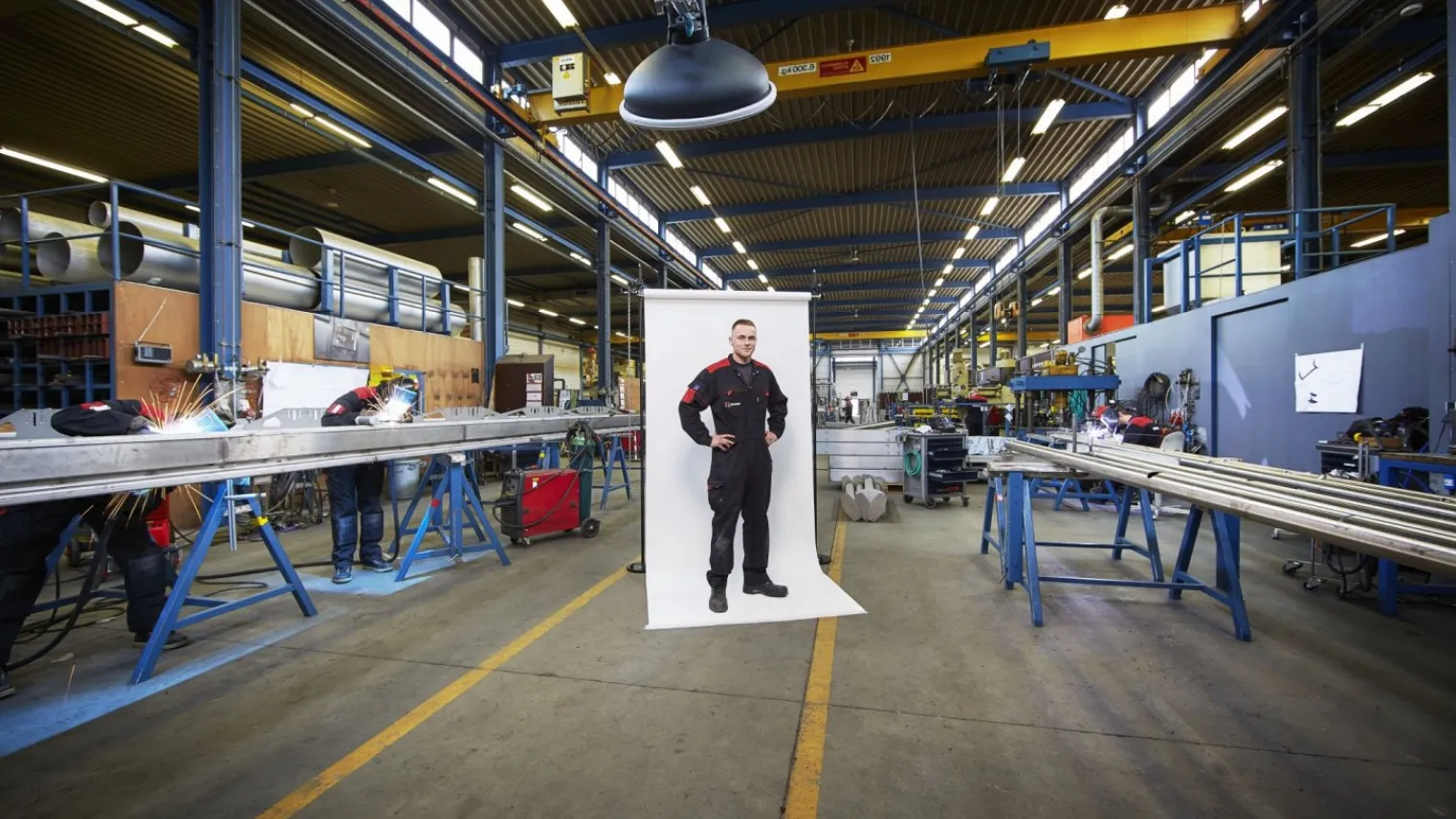 Student poseert op de werkplaats terwijl andere studenten aan het werk zijn
