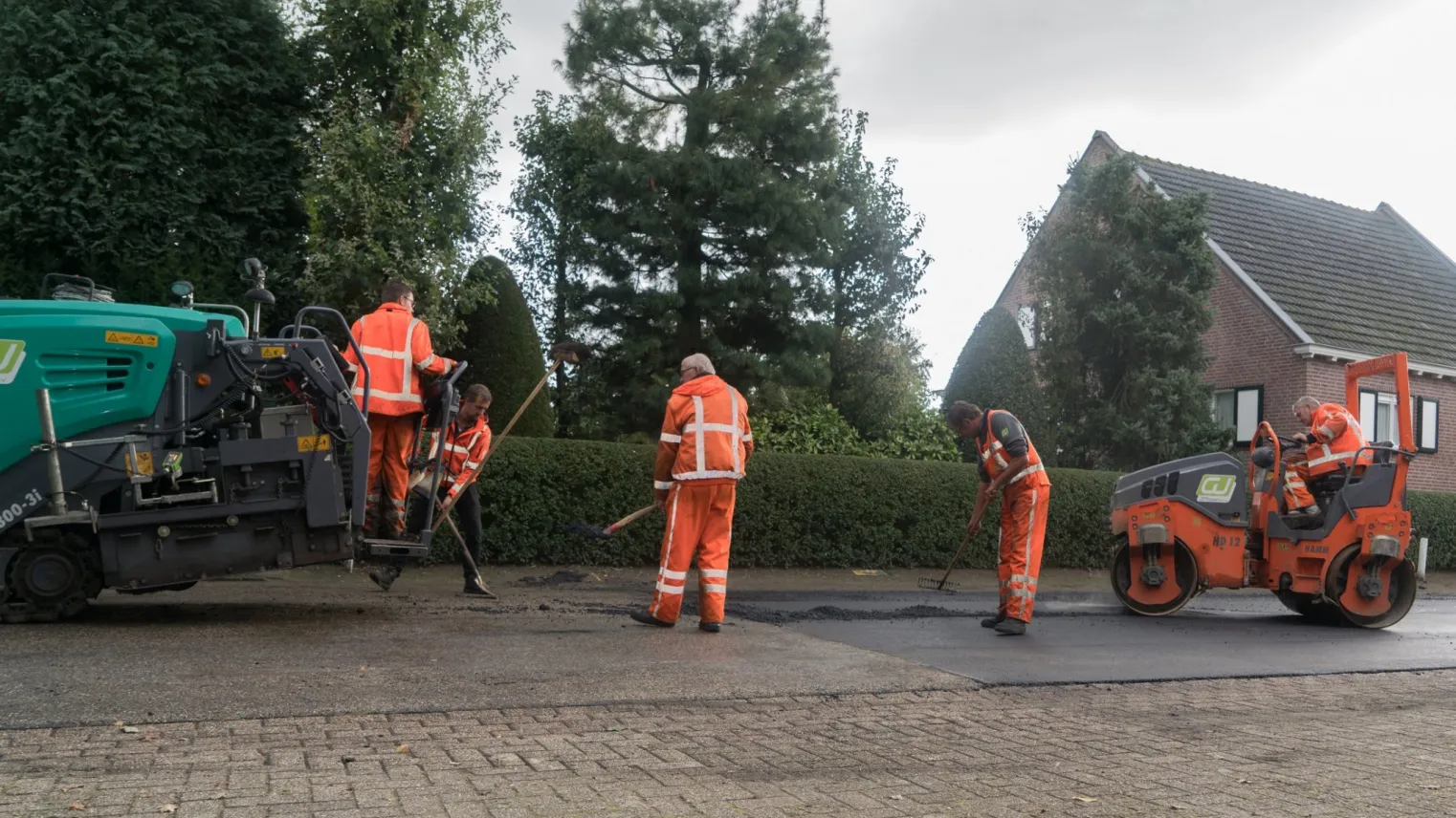 Groepje asfaltafwerkers werken samen aan de weg