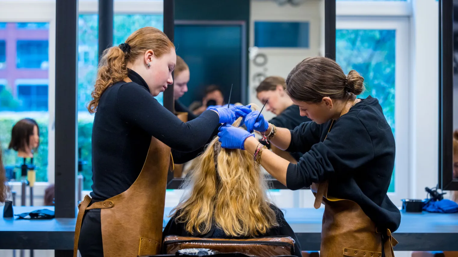 Twee dames stylen het haar van een vrouw in een kapsalon.