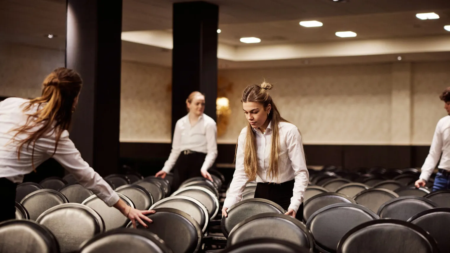 Facilitair dienstverleners zetten stoelen goed in zaal.