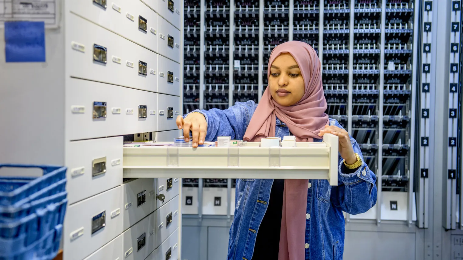 Een vrouw in een hijab kijkt naar een archiefkast in een apotheek.