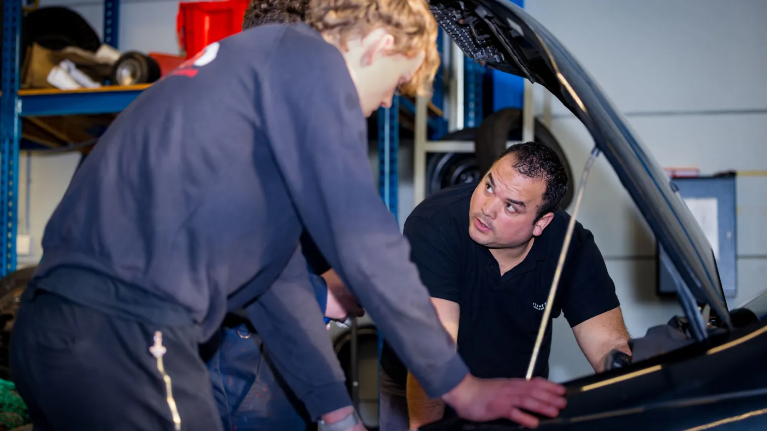 Leidinggevende automotive kijkt onder motorkap auto met twee collega's.