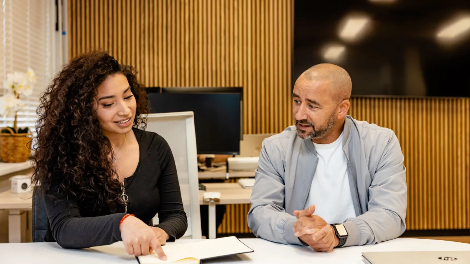 Medewerker in gesprek met begeleider praktijkleren aan een bureau.