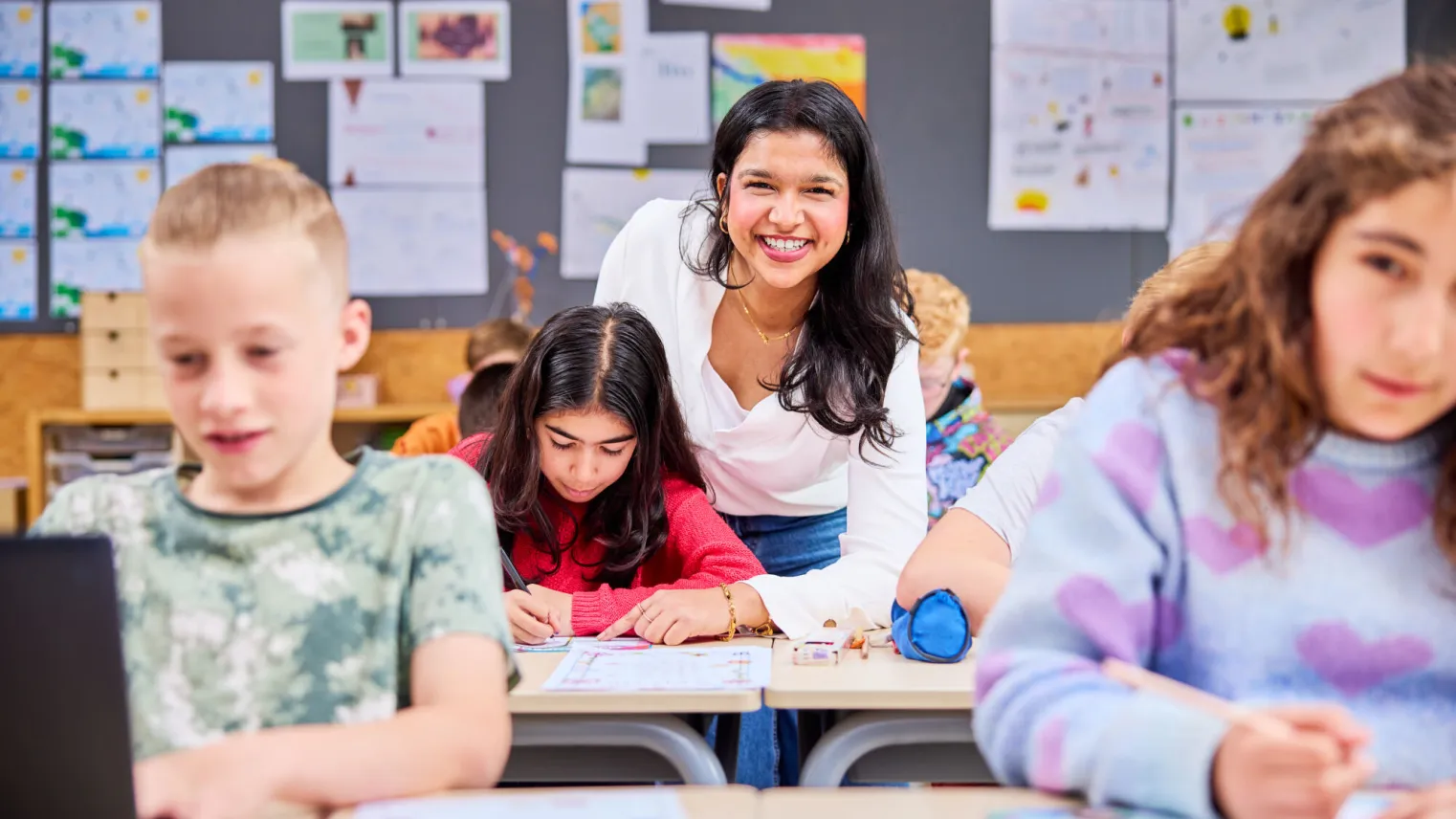 Onderwijsassistent kijkt mee bij schoolwerk basisschoolleerling