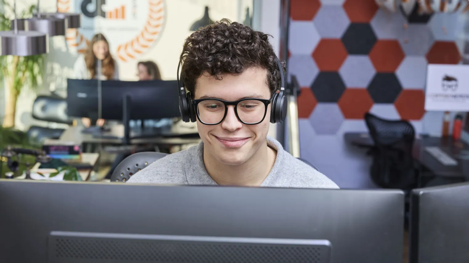 Student ICT werkt op computer met headset op