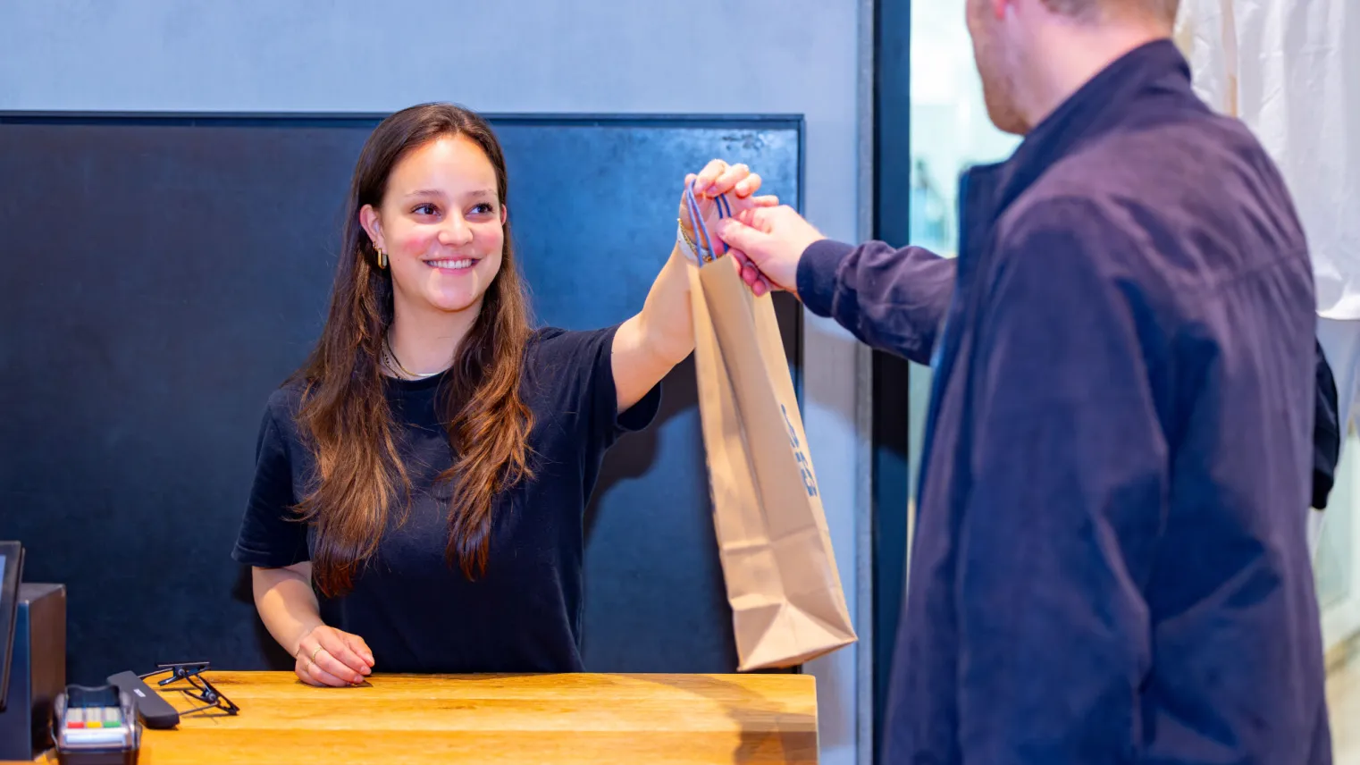 Student Retail overhandigt tasje aan klant bij de kassa