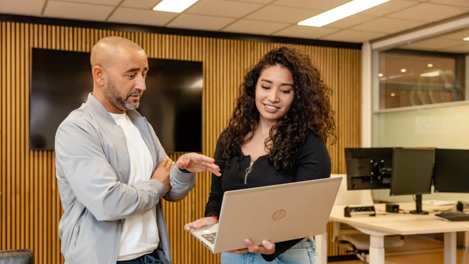 Student met laptop in haar hand aan het overleggen met docent.